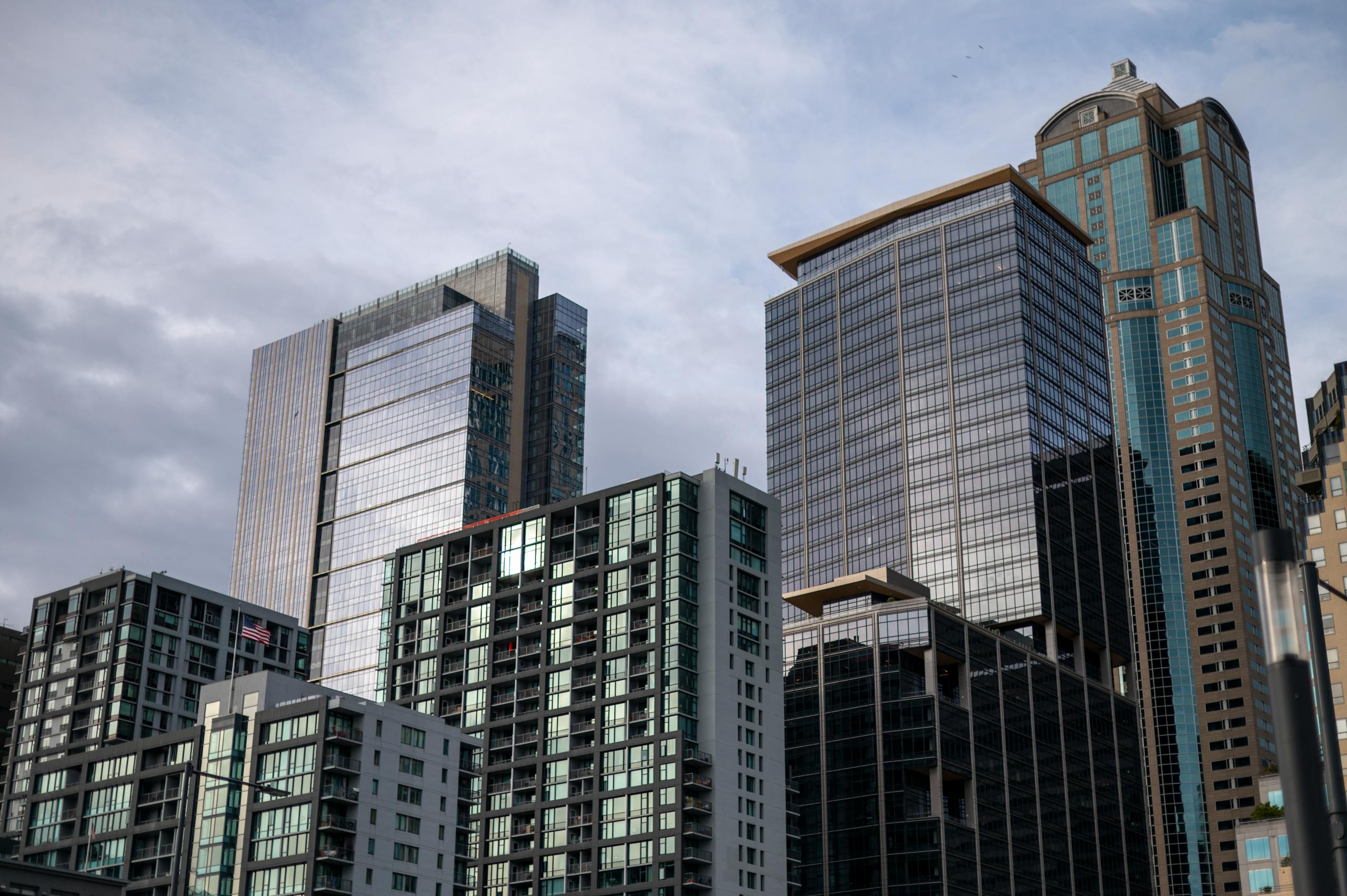 A cluster of modern skyscrapers with reflective glass facades set against a cloudy sky.