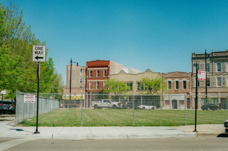 A street view in Chicago showing a vacant lot with surrounding buildings and clear blue sky.